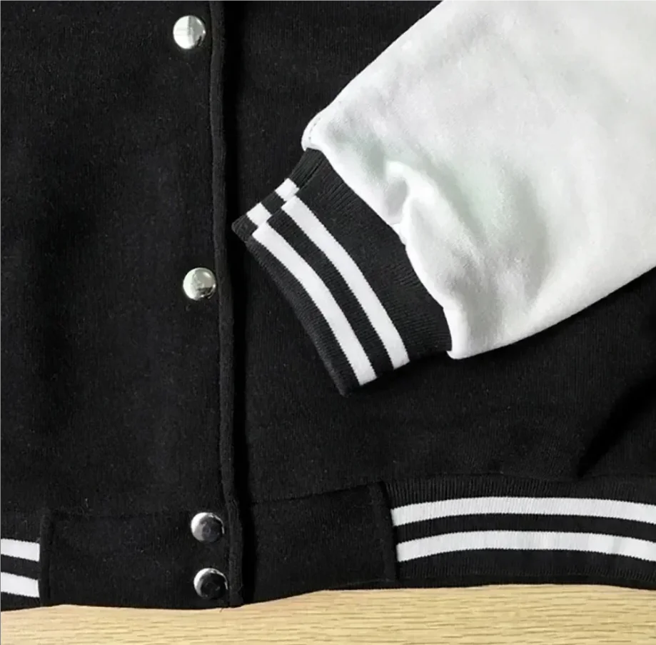 Black varsity jacket with white stripes on sleeves and collar, close-up on a wooden surface.