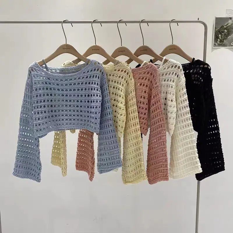 Row of colorful crochet sweaters on hangers against a white wall.