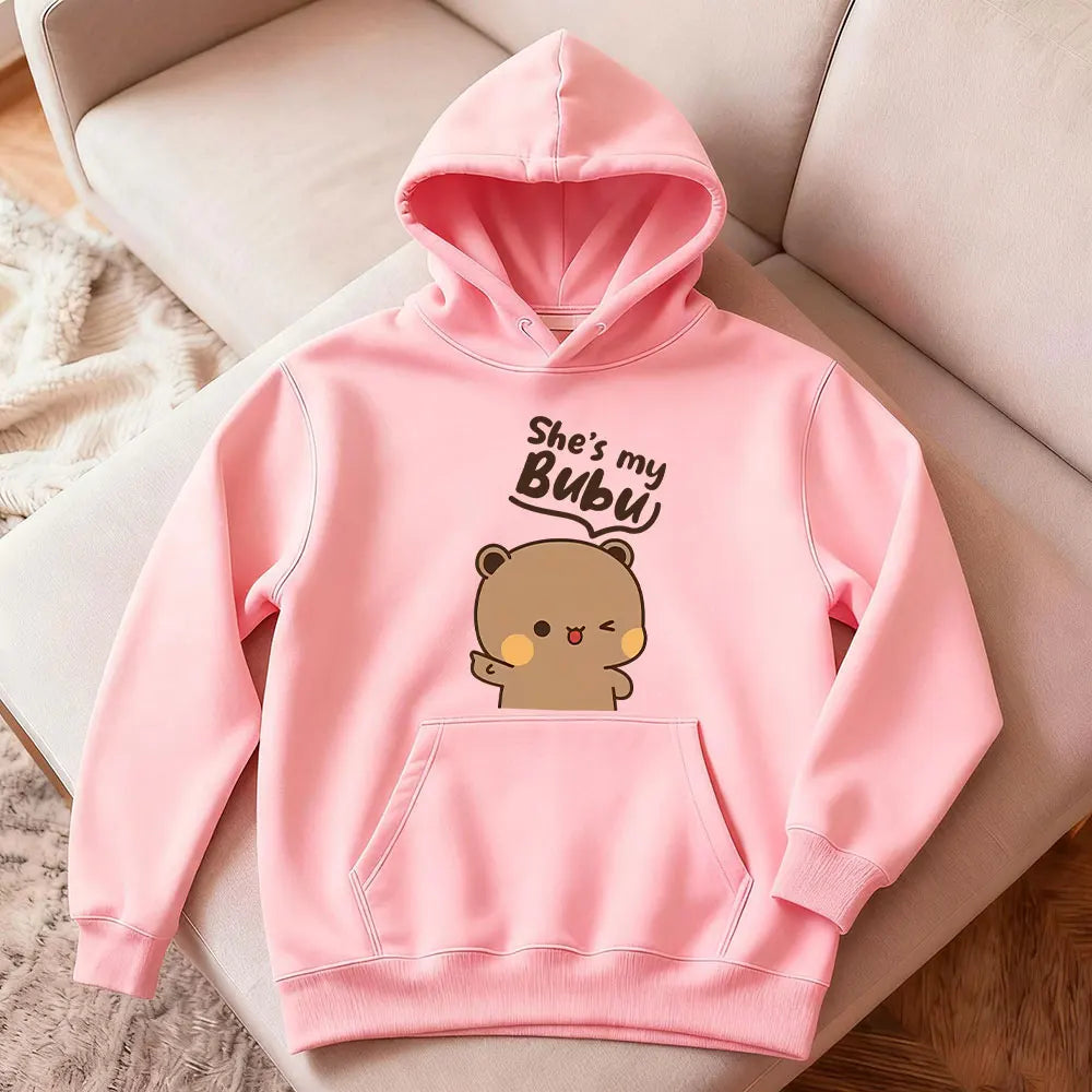 Pink hoodie with bear graphic and text on a beige chair
