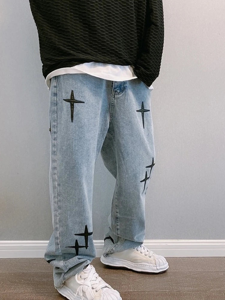 Person wearing light blue jeans with black star patterns and white sneakers against a plain background
