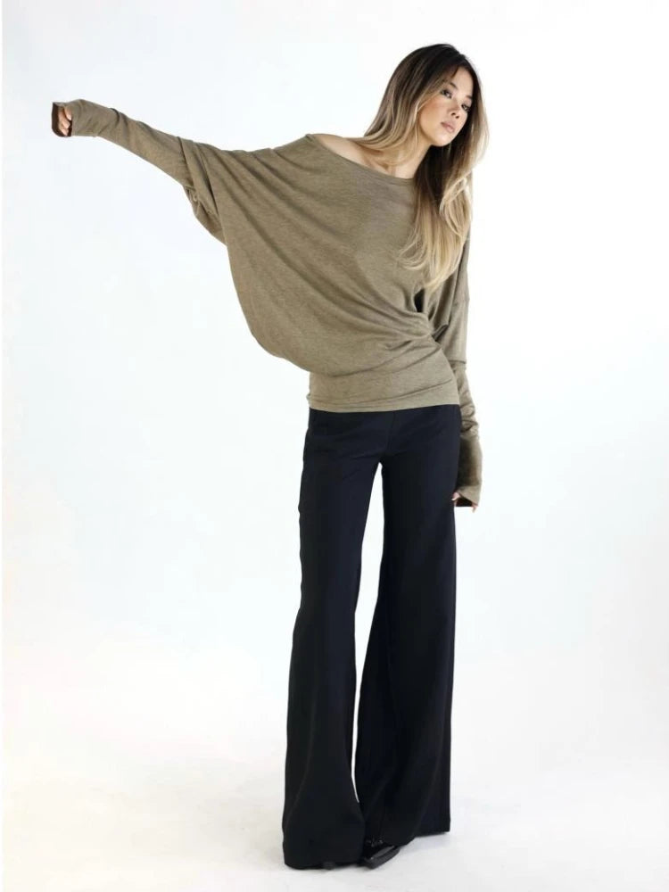 Woman wearing a loose-fitting beige sweater and black pants on a white background