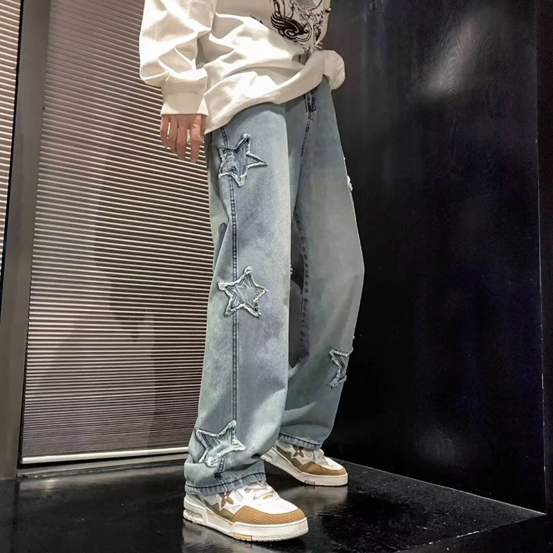 Person wearing light blue jeans with star patches and a white hoodie against a dark background.
