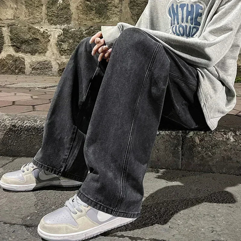 Person wearing a gray hoodie and dark jeans sitting on a stone ledge.