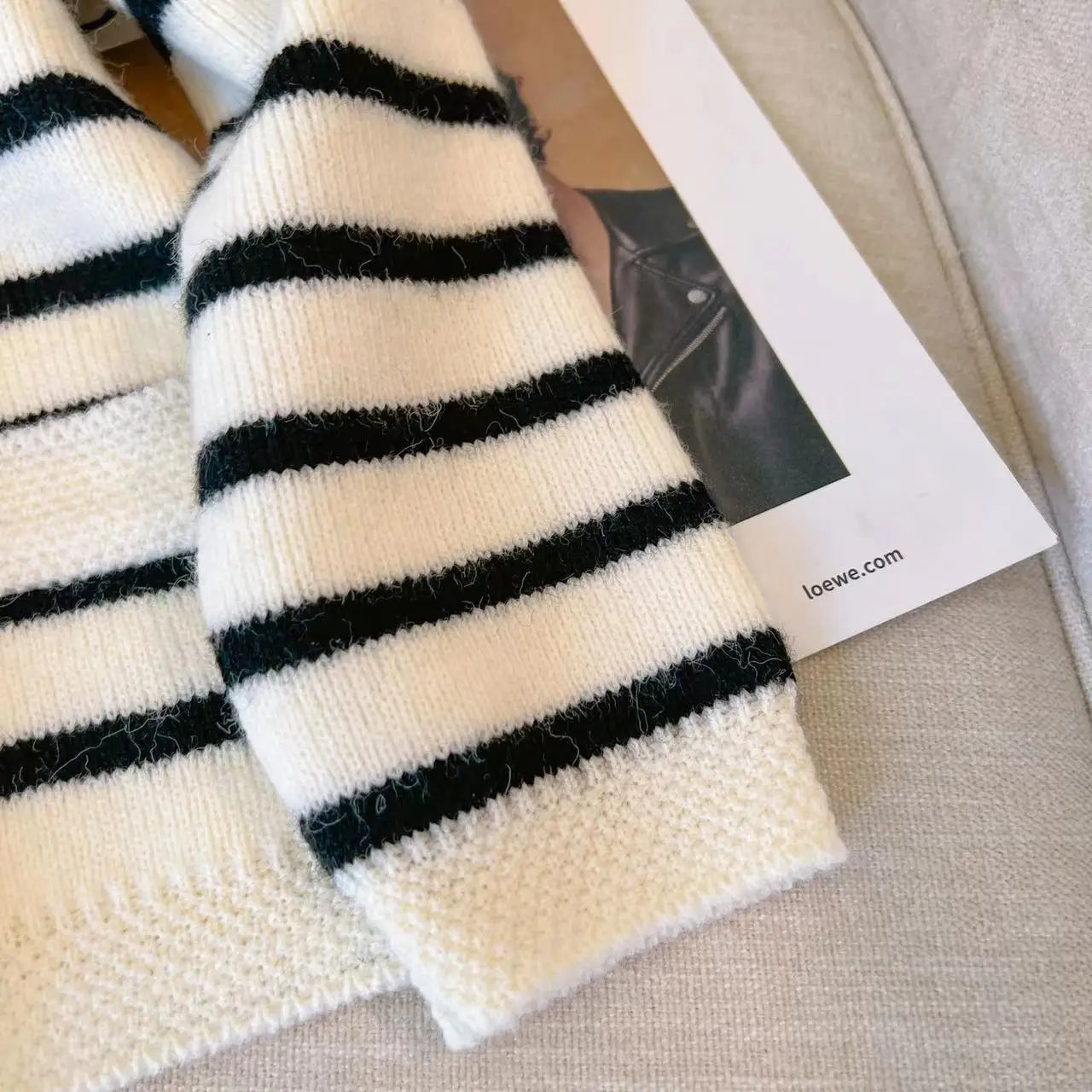 White and black striped scarf with a Loewe tag on a beige surface