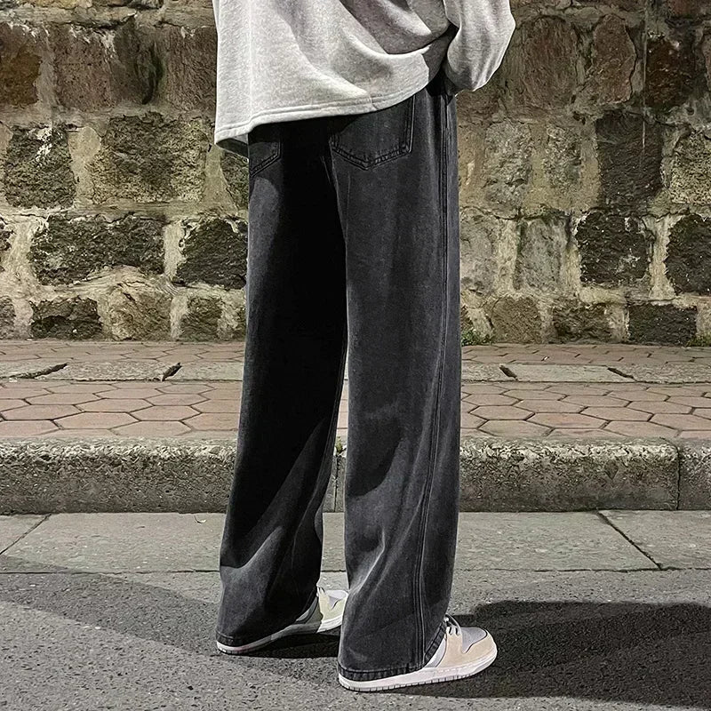 Person wearing black wide-leg jeans and a light gray sweatshirt against a stone wall.