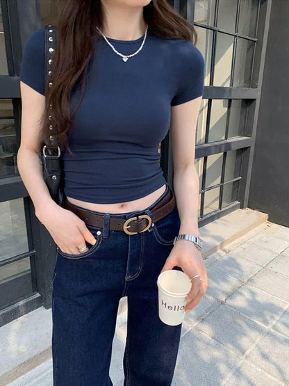 Person wearing a navy blue top and jeans, holding a coffee cup with a building in the background.