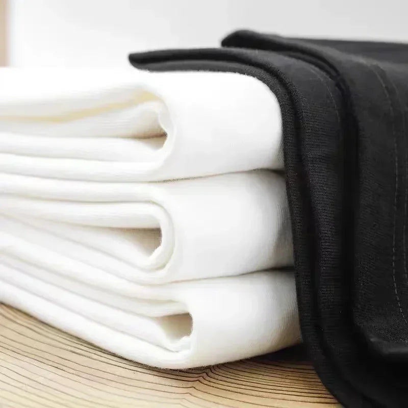 Stack of folded white and black t-shirts on a wooden surface.