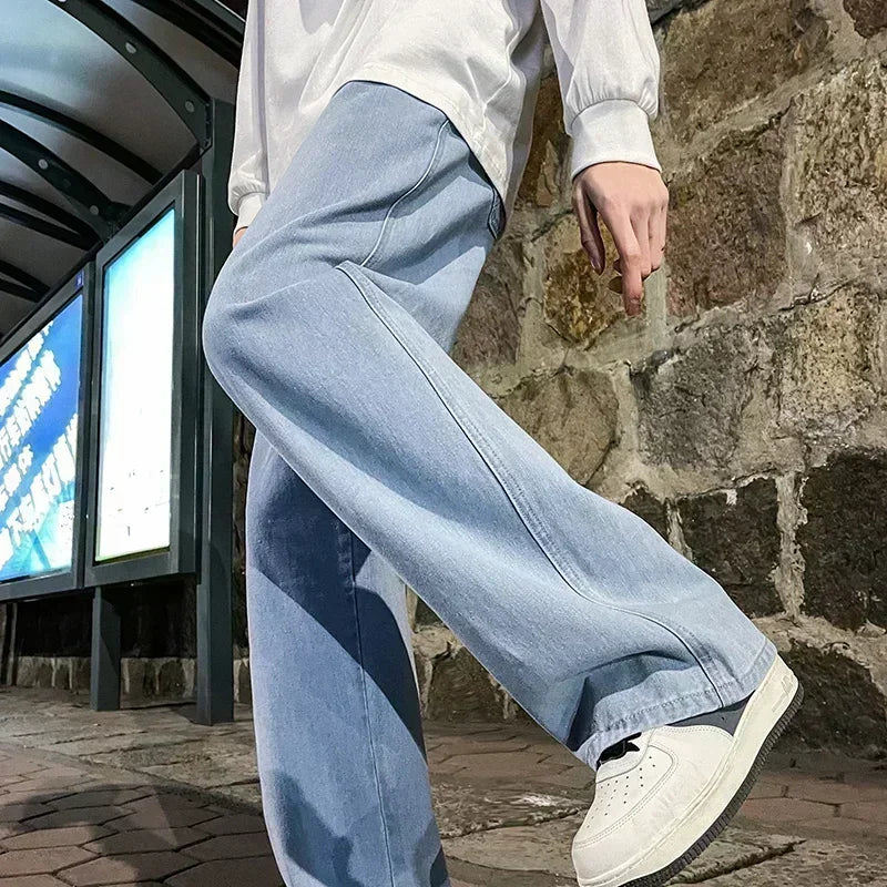 Person wearing light blue jeans and white sneakers in front of a stone wall.