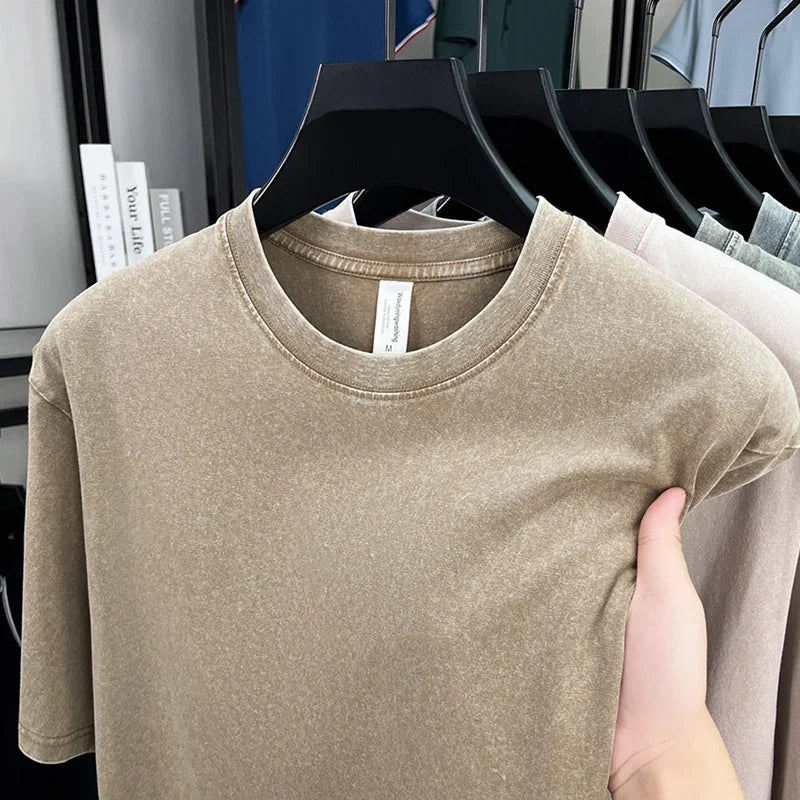 Beige t-shirt held by a hand with a clothing rack in the background