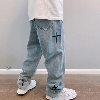Light blue jeans with black cross designs worn by a person against a plain wall.