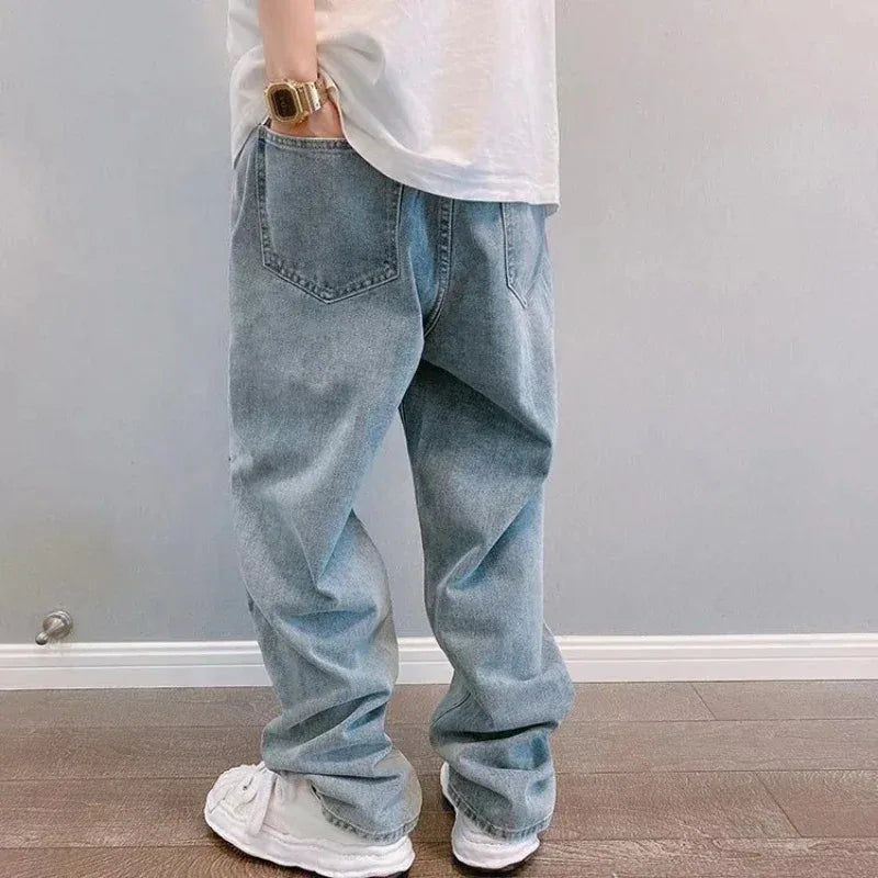 Person wearing light blue jeans and white sneakers against a plain wall.
