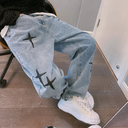 Light blue jeans with black star designs worn by a person sitting on a chair.