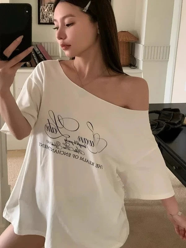 Woman wearing a white off-shoulder top with text, taking a mirror selfie.
