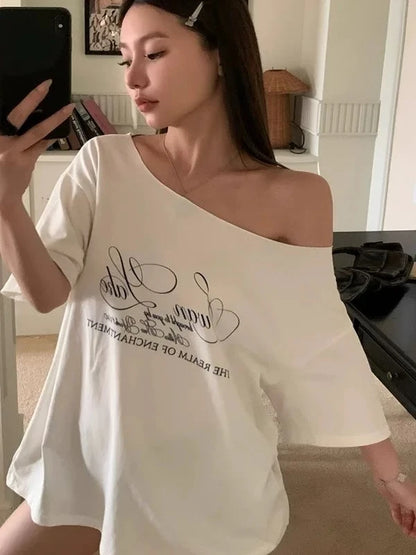 Woman wearing a white off-shoulder top with text, taking a mirror selfie.