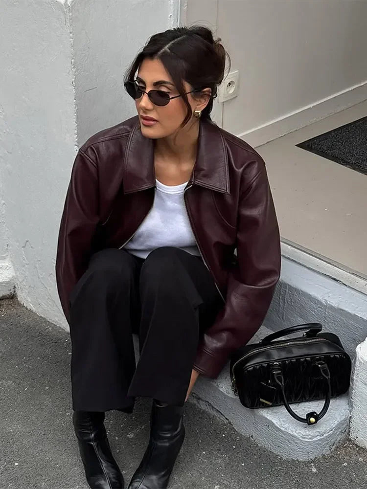 Woman sitting on a step wearing a brown leather jacket and black pants, with a black handbag beside her.