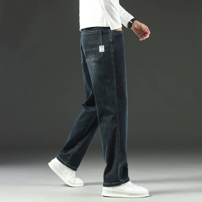 Person wearing dark blue jeans and white sneakers on a gray background
