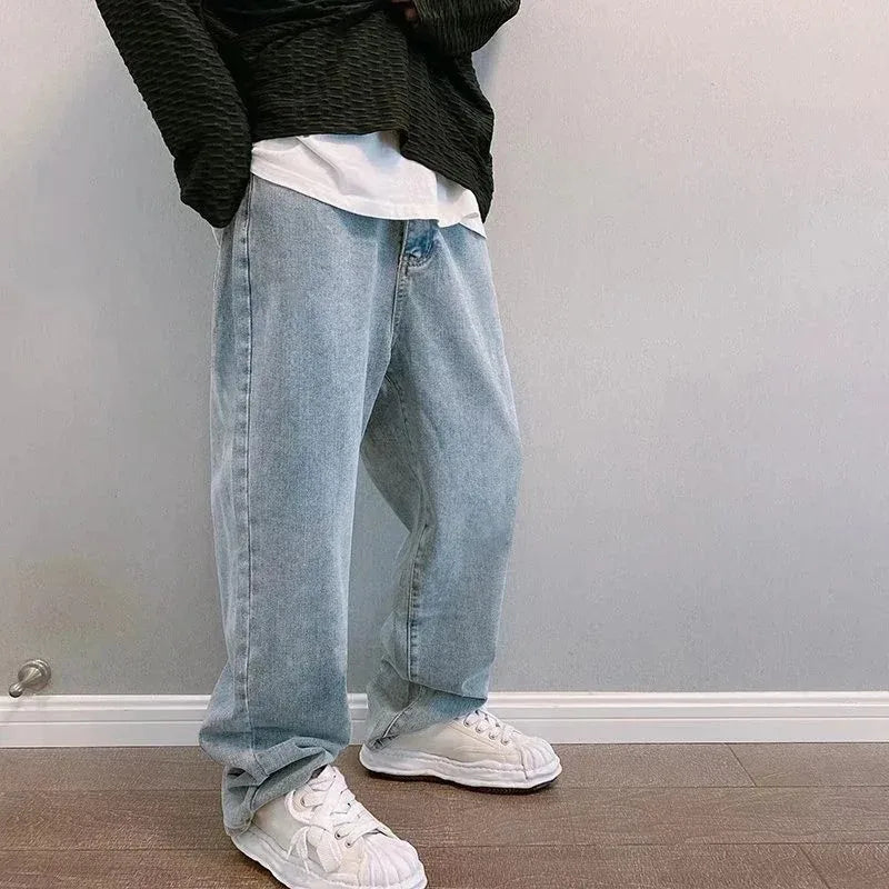 Person wearing light blue jeans and white sneakers against a plain wall.