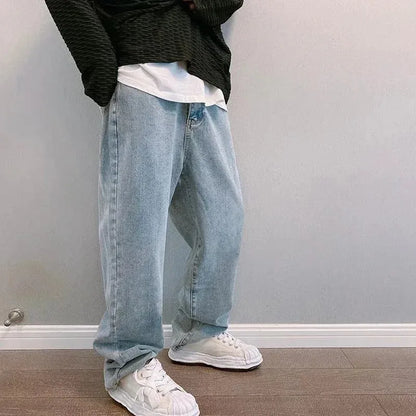 Person wearing light blue jeans and white sneakers against a plain wall.