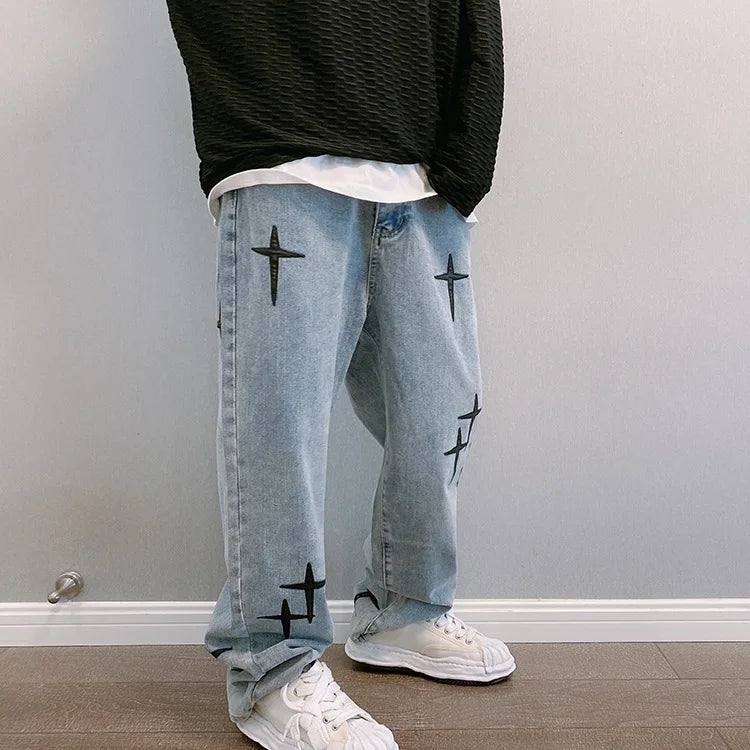 Person wearing light blue jeans with black star patterns and a black top against a plain wall.