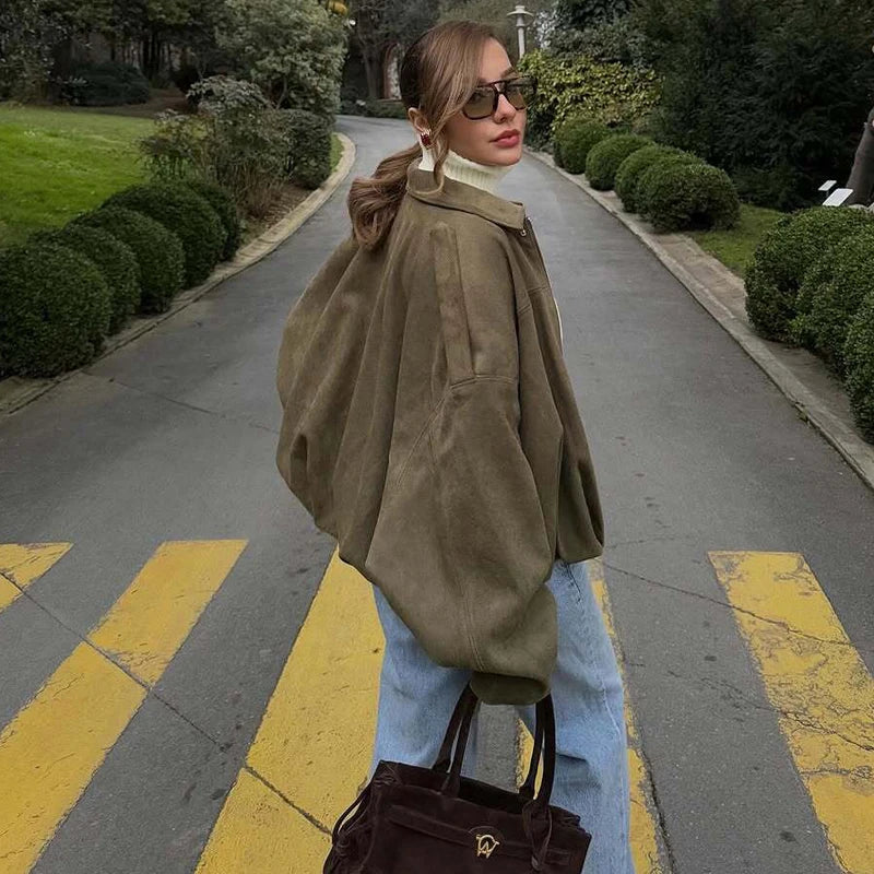 Woman in a brown coat and sunglasses crossing a zebra crossing in a park-like setting.