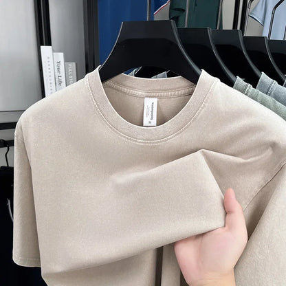 Beige t-shirt held by a hand with a clothing rack in the background