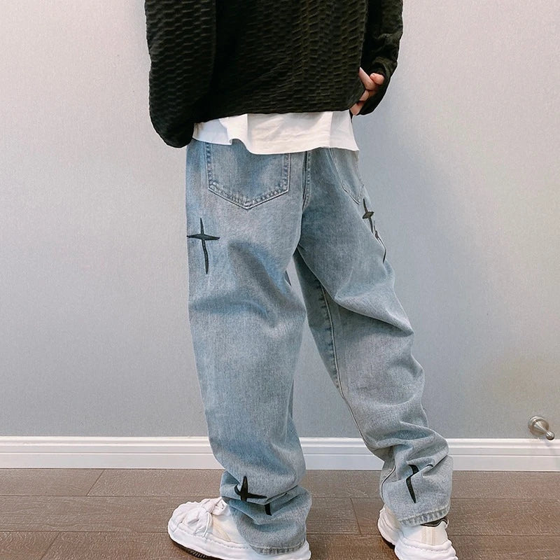 Person wearing light blue jeans with star designs and a black textured sweater in an indoor setting.