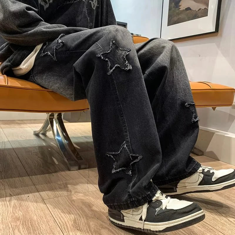 Person wearing black distressed jeans with star patches and black and white sneakers in a room.
