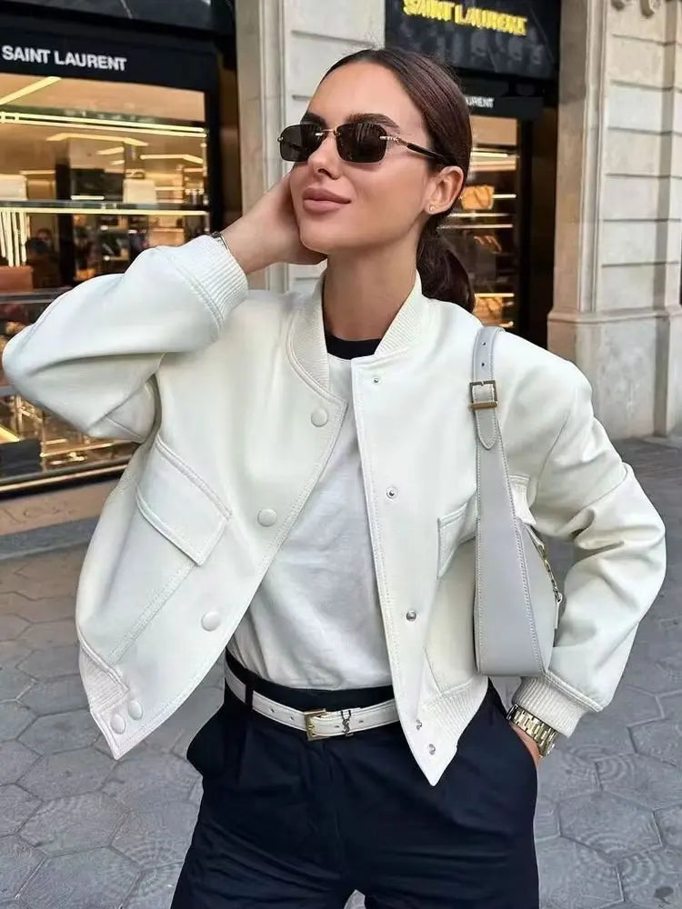 Woman wearing a white jacket and sunglasses in front of a store entrance.