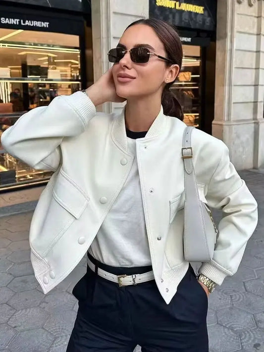 Woman wearing a white jacket and sunglasses in front of a store entrance.