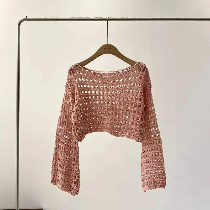 Pink crochet sweater on a hanger against a plain background