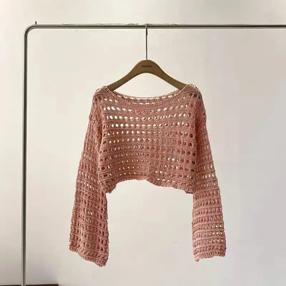 Pink crochet sweater on a hanger against a plain background