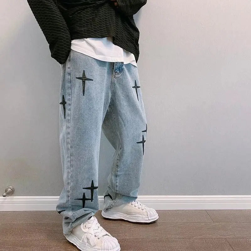 Person wearing light blue jeans with black star patterns and white sneakers against a plain wall.