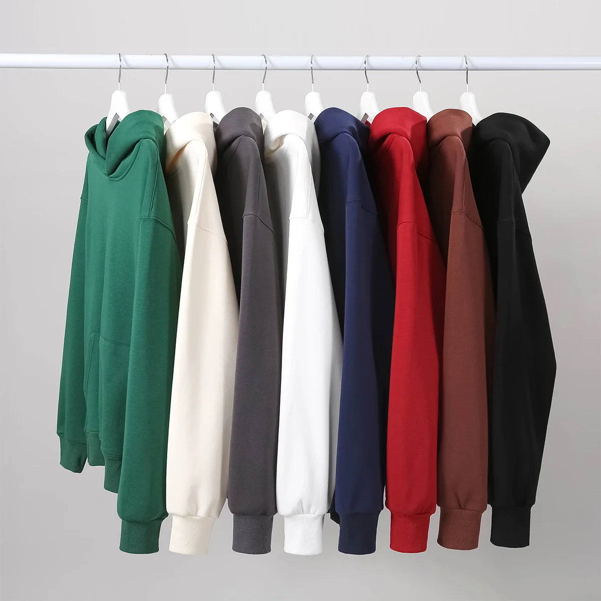 Row of colorful hoodies on hangers against a plain background