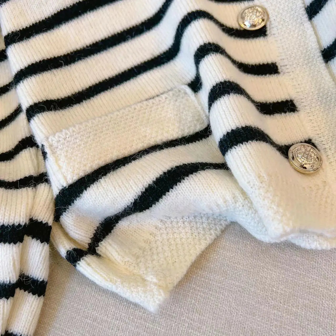 Close-up of a black and white striped cardigan with buttons on a beige surface