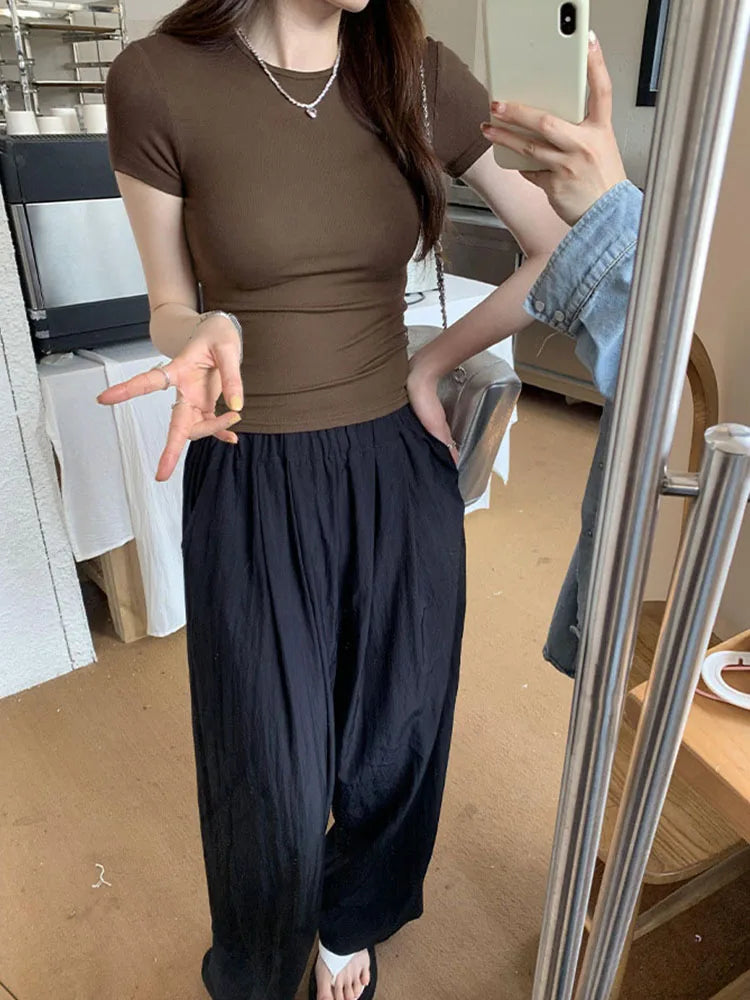Person wearing a brown top and black pants taking a mirror selfie.