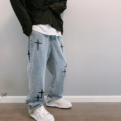 Person wearing light blue jeans with black star patterns and white sneakers against a plain wall.