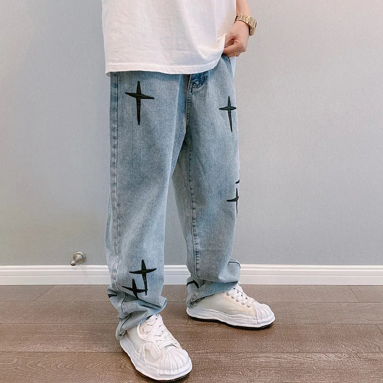 Person wearing light blue jeans with black star patterns and white sneakers in a room.
