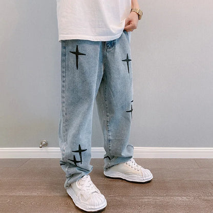 Person wearing light blue jeans with black star patterns and white sneakers in a room.