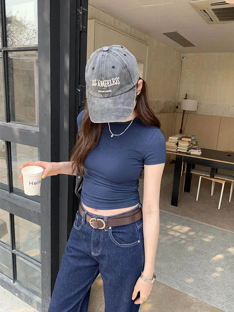 Person wearing a blue top and jeans, holding a cup, standing in a modern interior setting.