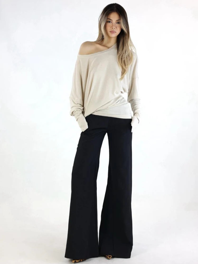 Woman wearing a beige off-shoulder top and black wide-leg pants on a white background