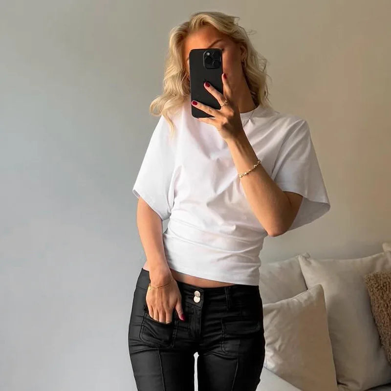 Person taking a mirror selfie wearing a white top and black pants in a living room.