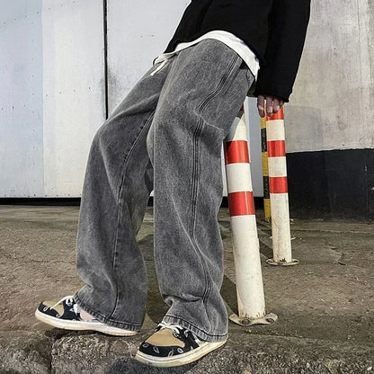 Person wearing gray jeans and black sneakers leaning against a pole with a concrete wall background