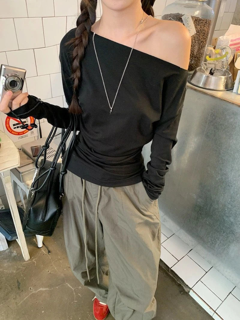 Person wearing a black off-shoulder top and beige pants in an indoor setting.