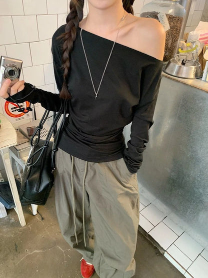 Person wearing a black off-shoulder top and beige pants in an indoor setting.