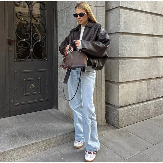 Woman holding a brown leather bag against a stone building.